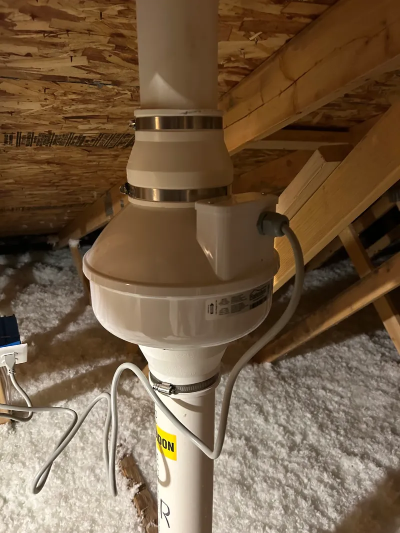 Radon fan mounted in the attic on a labeled radon vent pipe
