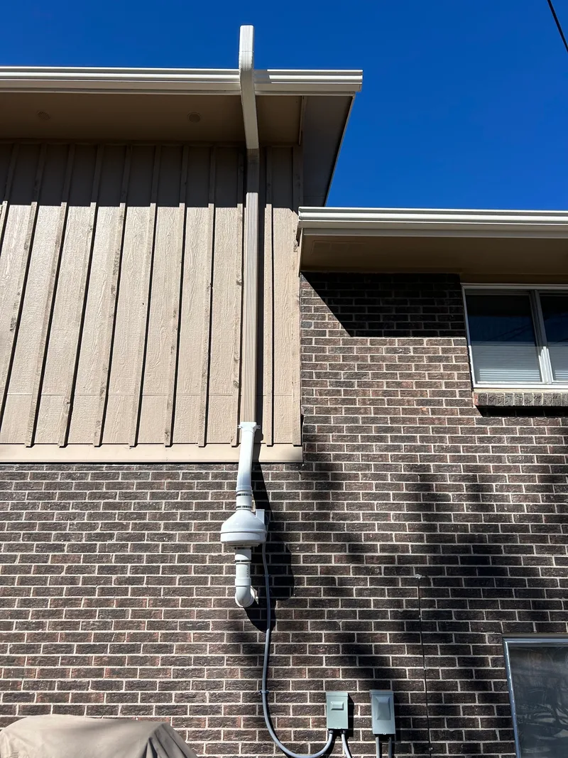 Radon fan on a two-story brick home with the downspout matched to the upper siding