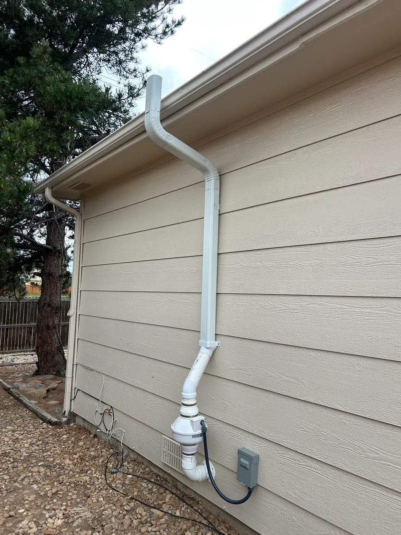 Exterior radon fan with a downspout run offset around the eave on tan siding