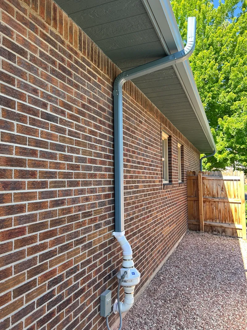 Gray downspout radon run with fan at grade on a brick wall