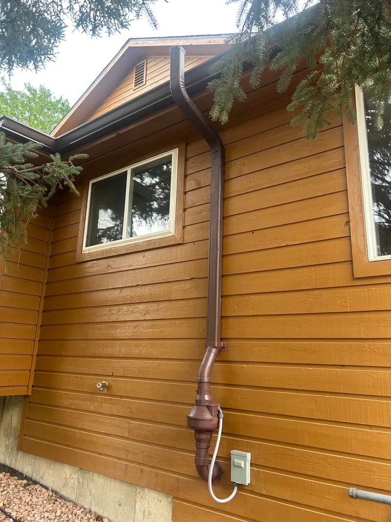 Full-height Royal Brown downspout radon run color-matched to golden-brown lap siding
