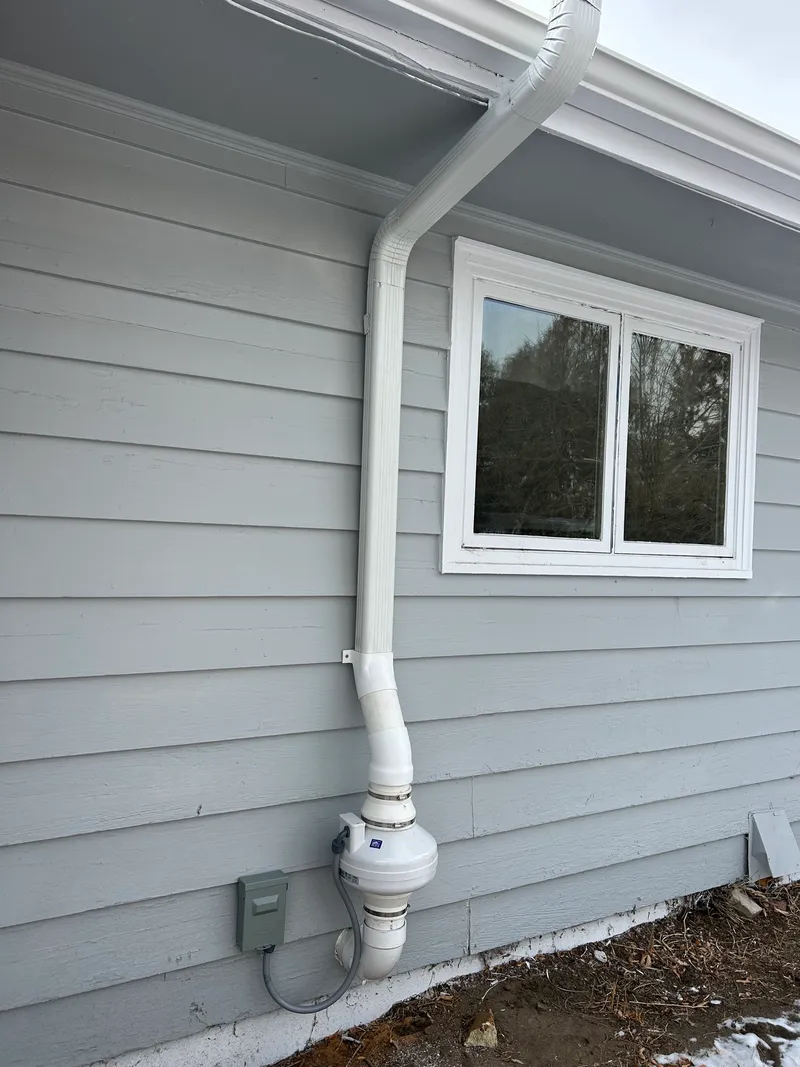 White downspout radon run and exterior fan on gray lap siding